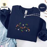 Navy crewneck sweatshirt folded with ripped jeans and a silver chain necklace, embroidered with four black and tan dachshunds in Santa hats leaping between mistletoe sprigs with red bows and silver snowflakes