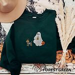 Forest Green crewneck sweatshirt laid flat with a brown hat and pampas grass, embroidered with a red dachshund in a skeleton costume and witch hat on a leash held by a ghost sipping iced coffee