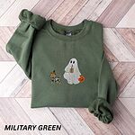 Military Green crewneck sweatshirt laid flat on a wood floor, embroidered with a red dachshund in a skeleton costume and witch hat on a leash held by a ghost sipping iced coffee