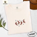 Ivory Comfort Colors T-shirt embroidered with four red dachshunds in red Fair Isle sweaters tumbling among light blue snowflakes