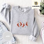 Ash crewneck sweatshirt folded with denim shorts, white sneakers and a potted plant, embroidered with four red dachshunds in red Fair Isle sweaters tumbling among light blue snowflakes