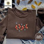 Dark Chocolate crewneck sweatshirt on a plaid flannel shirt with yellow autumn leaves and denim shorts, embroidered with four red dachshunds in red Fair Isle sweaters tumbling among light blue snowflakes