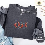 Dark Heather crewneck sweatshirt folded with ripped jeans and a silver chain necklace, embroidered with four red dachshunds in red Fair Isle sweaters tumbling among light blue snowflakes