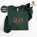 Forest Green crewneck sweatshirt folded on a white background, embroidered with four red dachshunds in red Fair Isle sweaters tumbling among light blue snowflakes