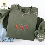 Military Green crewneck sweatshirt folded with light jeans and a silver chain necklace, embroidered with four red dachshunds in red Fair Isle sweaters tumbling among light blue snowflakes