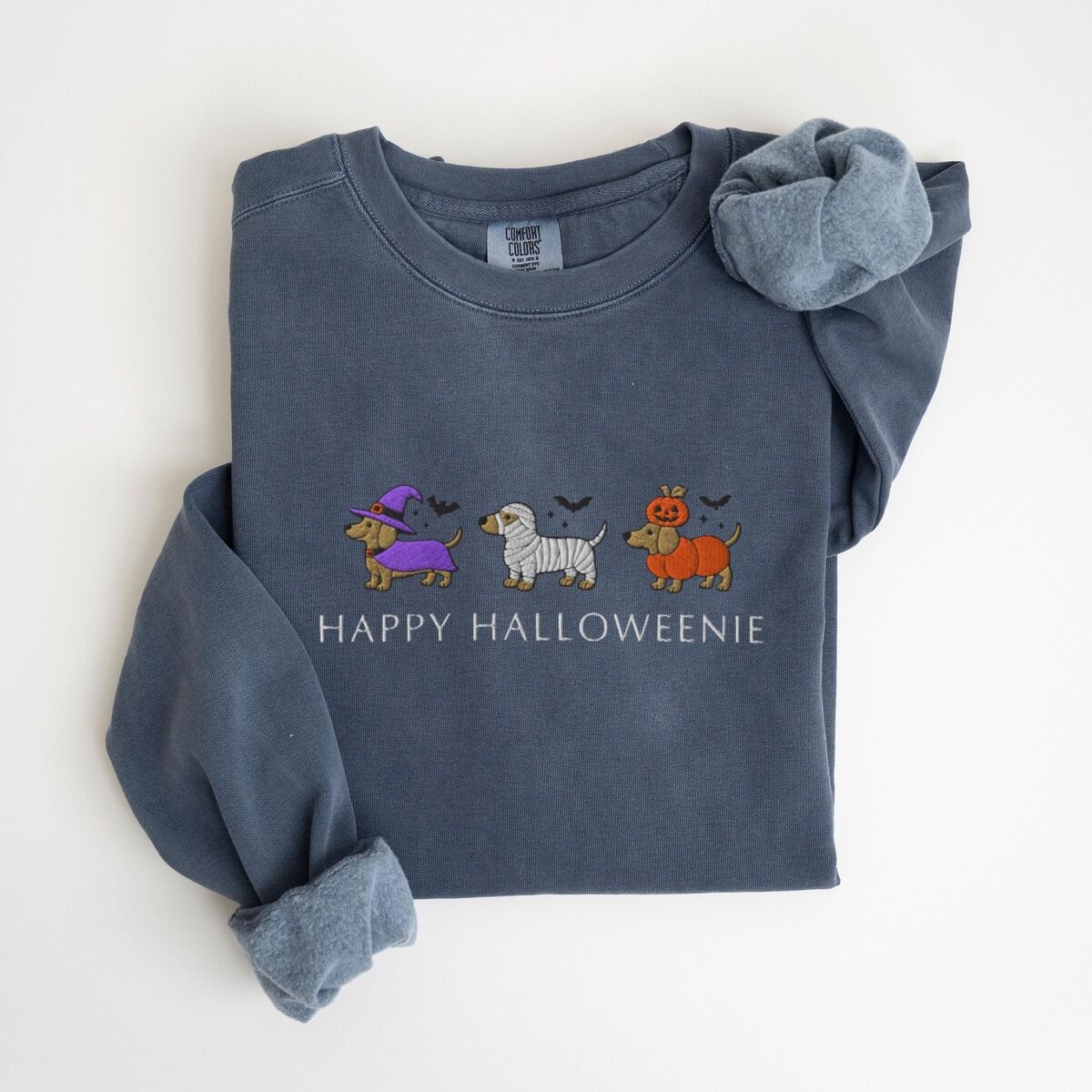 Dachshunds in Halloween Costumes Sweatshirt – Denim Denim crewneck sweatshirt laid flat on white, embroidered with three dachshunds dressed as a witch, a mummy and a pumpkin with bats overhead, above the words HAPPY HALLOWEENIE