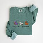 Light Green crewneck sweatshirt laid flat on white, embroidered with three dachshunds dressed as a witch, a mummy and a pumpkin with bats overhead, above the words HAPPY HALLOWEENIE