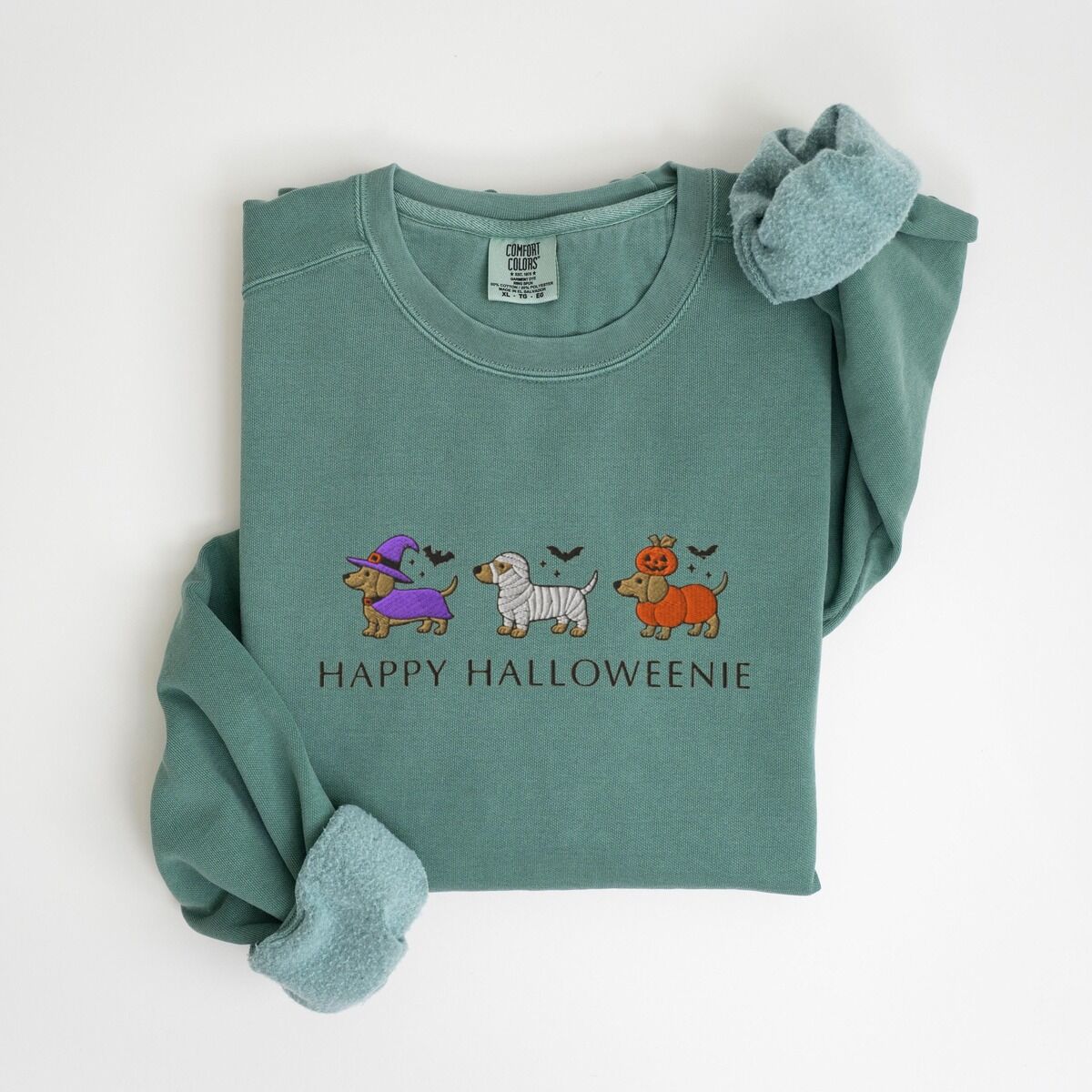 Dachshunds in Halloween Costumes Sweatshirt – Light Green Light Green crewneck sweatshirt laid flat on white, embroidered with three dachshunds dressed as a witch, a mummy and a pumpkin with bats overhead, above the words HAPPY HALLOWEENIE