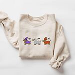 Sand crewneck sweatshirt laid flat on white, embroidered with three dachshunds dressed as a witch, a mummy and a pumpkin with bats overhead