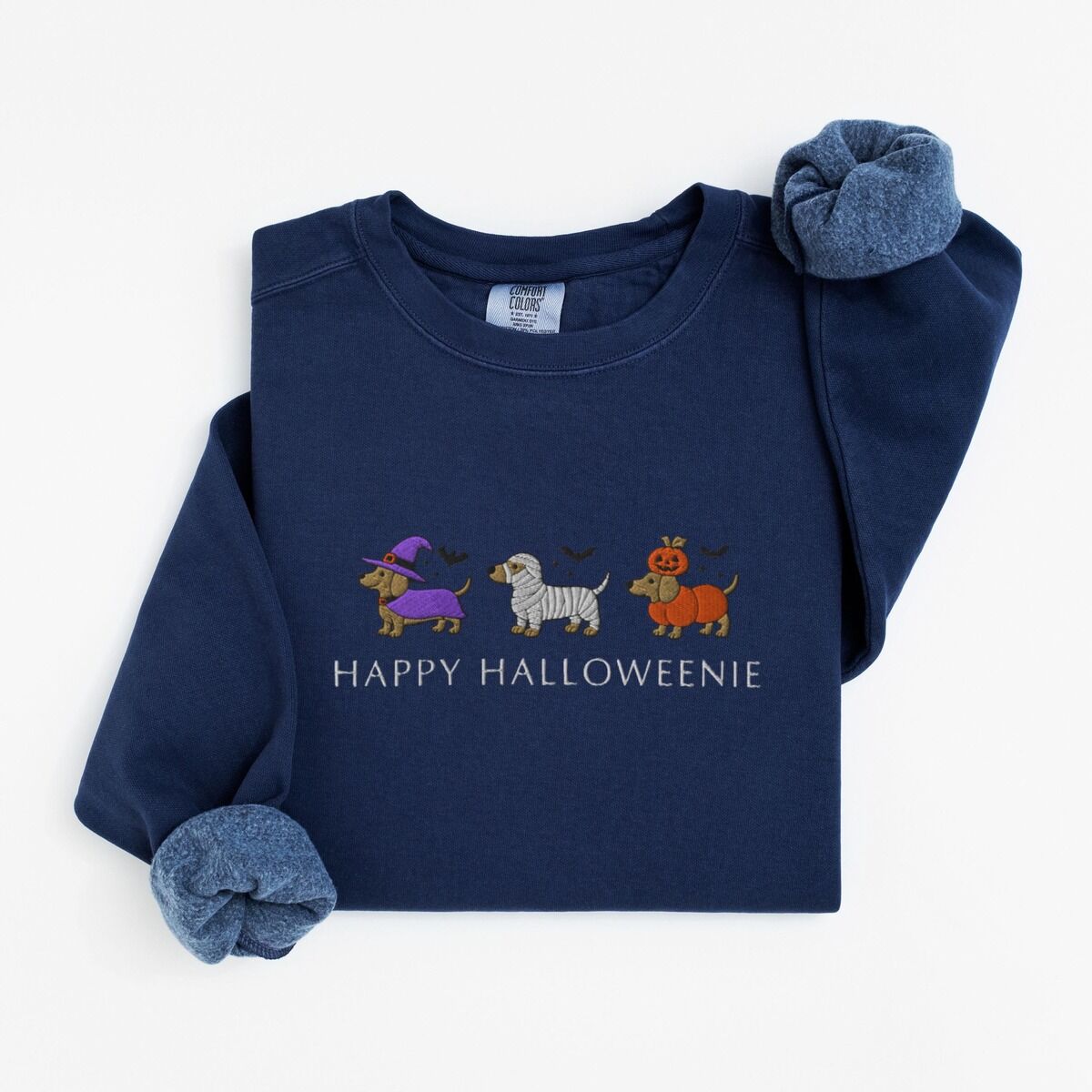 Dachshunds in Halloween Costumes Sweatshirt – True Navy True Navy crewneck sweatshirt laid flat on white, embroidered with three dachshunds dressed as a witch, a mummy and a pumpkin with bats overhead, above the words HAPPY HALLOWEENIE