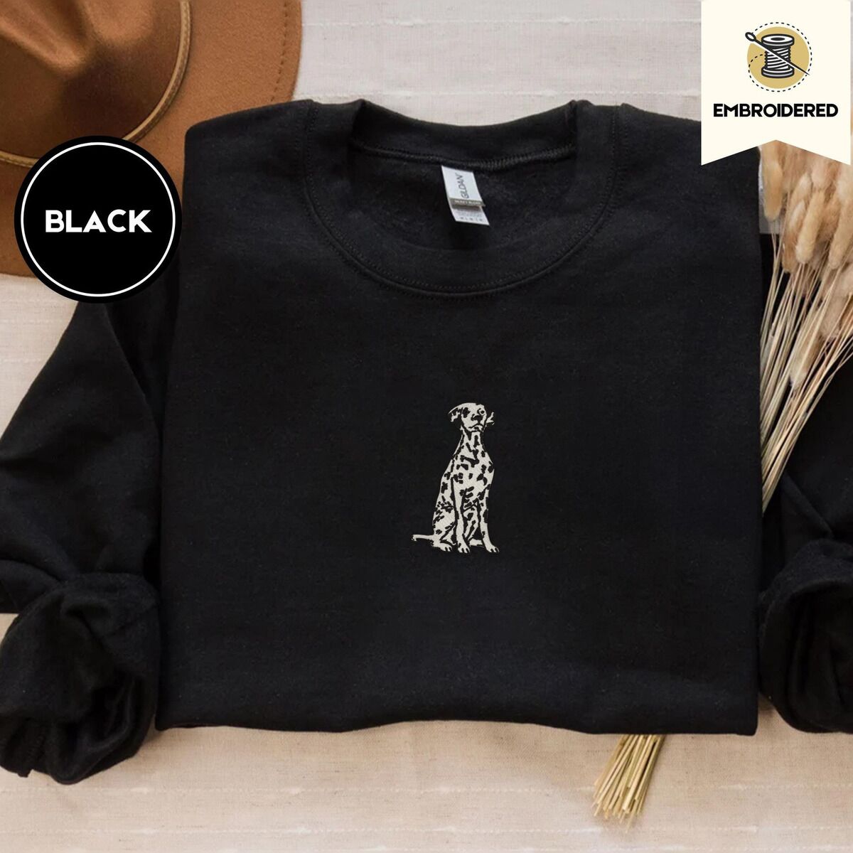 Dalmatian Sweatshirt – Black Black crewneck sweatshirt with a brown felt hat and dried bunny tail grass, embroidered with a sitting Dalmatian in white with black spots and a black outline