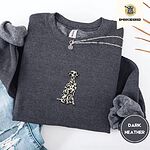 Dark Heather crewneck sweatshirt folded with ripped jeans and a silver chain necklace, embroidered with a sitting Dalmatian in white with black spots and a black outline