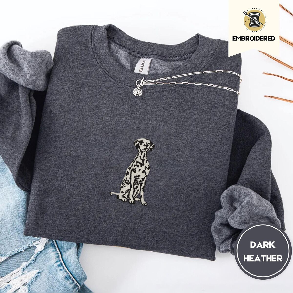 Dalmatian Sweatshirt – Dark Heather Dark Heather crewneck sweatshirt folded with ripped jeans and a silver chain necklace, embroidered with a sitting Dalmatian in white with black spots and a black outline