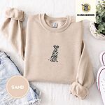 Sand crewneck sweatshirt folded with denim shorts, white sneakers and a potted plant, embroidered with a sitting Dalmatian in white with black spots and a black outline