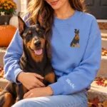 Doberman mom wearing the Heather Deep Royal Halloween sweatshirt with her Doberman Pinscher on a fall porch