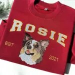 Dog face Christmas sweatshirt in maroon with an embroidered Australian shepherd portrait, the name ROSIE in white varsity letters and EST 2021