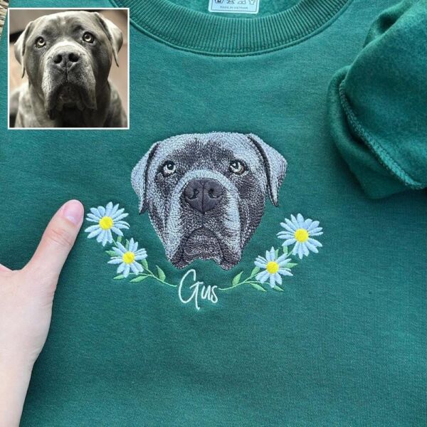 Forest green dog memorial sweatshirt with an embroidered gray dog portrait, a white daisy wreath and the name Gus in white script, beside the original photo