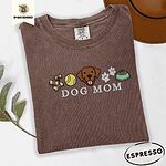 Espresso Comfort Colors T-shirt embroidered with a row of dog treats, a tennis ball, a chocolate Lab face, paw prints and a food bowl above the words DOG MOM