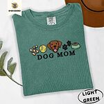 Light Green Comfort Colors T-shirt embroidered with a row of dog treats, a tennis ball, a chocolate Lab face, paw prints and a food bowl above the words DOG MOM