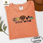 Terracotta Comfort Colors T-shirt embroidered with a row of dog treats, a tennis ball, a chocolate Lab face, paw prints and a food bowl above the words DOG MOM