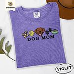 Violet Comfort Colors T-shirt embroidered with a row of dog treats, a tennis ball, a chocolate Lab face, paw prints and a food bowl above the words DOG MOM