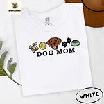 White Comfort Colors T-shirt embroidered with a row of dog treats, a tennis ball, a chocolate Lab face, paw prints and a food bowl above the words DOG MOM