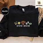 Black crewneck sweatshirt with a brown felt hat and dried bunny tail grass, embroidered with a row of dog treats, a tennis ball, a chocolate Lab face, paw prints and a food bowl above the words DOG MOM
