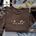 Dark Chocolate crewneck sweatshirt on a plaid flannel shirt with yellow autumn leaves and denim shorts, embroidered with a row of dog treats, a tennis ball, a chocolate Lab face, paw prints and a food bowl above the words DOG MOM