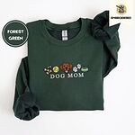 Forest Green crewneck sweatshirt folded on a white background, embroidered with a row of dog treats, a tennis ball, a chocolate Lab face, paw prints and a food bowl above the words DOG MOM