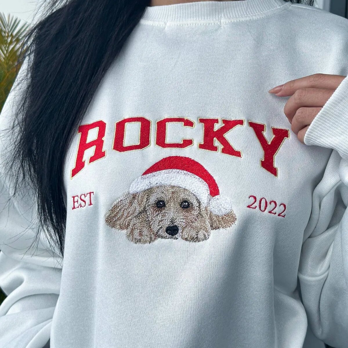 Dog Name Christmas Sweatshirt Worn Woman wearing a white custom dog Christmas sweatshirt with ROCKY varsity letters and EST 2022
