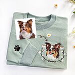 Light green crewneck sweatshirt with a full-color embroidered portrait of an Australian Shepherd in a white daisy wreath above the name Emma, a paw print on the sleeve, beside the original dog photo