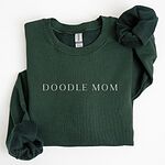 Forest Green crewneck sweatshirt laid flat with a rolled cuff, embroidered with DOODLE MOM in thin serif capitals across the chest