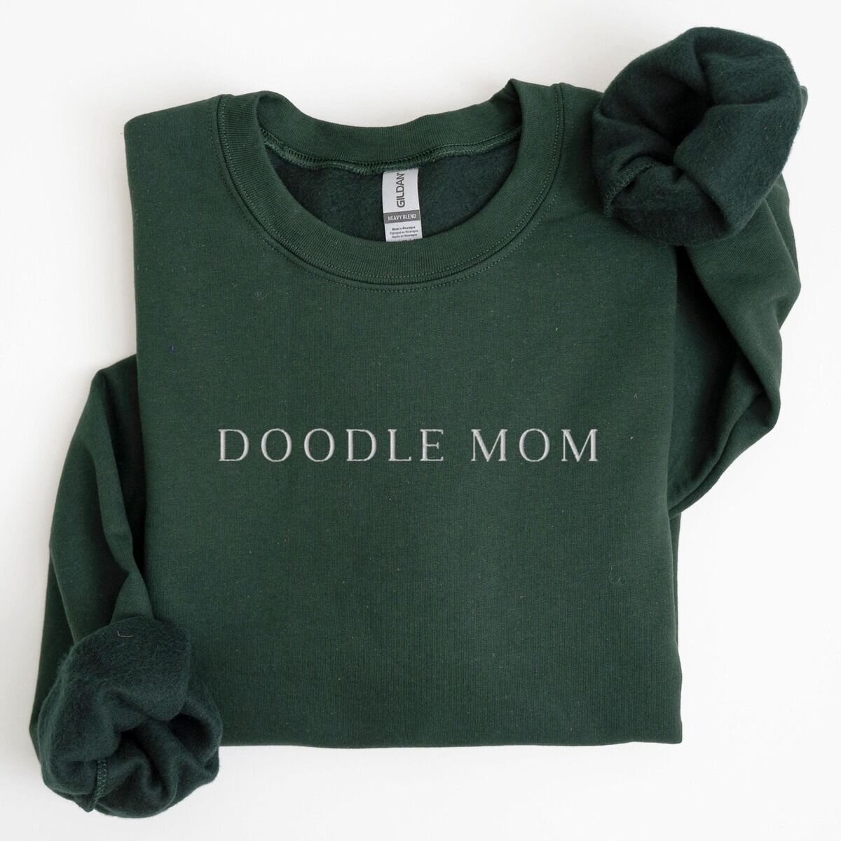 Doodle Mom Crewneck – Forest Green Forest Green crewneck sweatshirt laid flat with a rolled cuff, embroidered with DOODLE MOM in thin serif capitals across the chest