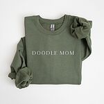 Military Green crewneck sweatshirt laid flat with a rolled cuff, embroidered with DOODLE MOM in light serif capitals across the chest