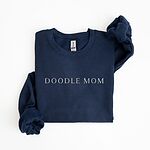 Navy crewneck sweatshirt laid flat with a rolled cuff, embroidered with DOODLE MOM in light serif capitals across the chest