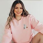 Smiling woman in a Light Pink crewneck sweatshirt embroidered on the left chest with a ghost sipping red wine, a black and tan dachshund and a jack-o'-lantern