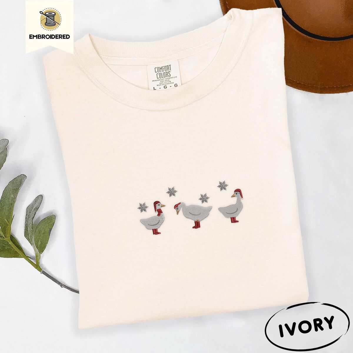 Duck in Boots Shirt – Ivory Ivory Comfort Colors T-shirt embroidered with three white ducks in Santa hats and red rain boots under silver snowflakes