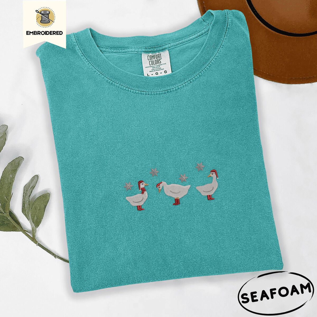 Duck in Boots Shirt – Seafoam Seafoam Comfort Colors T-shirt embroidered with three white ducks in Santa hats and red rain boots under silver snowflakes