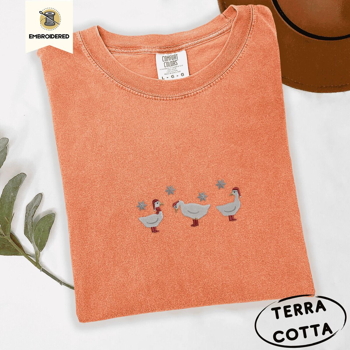Duck in Boots Shirt – Terracotta Terracotta Comfort Colors T-shirt embroidered with three white ducks in Santa hats and red rain boots under silver snowflakes