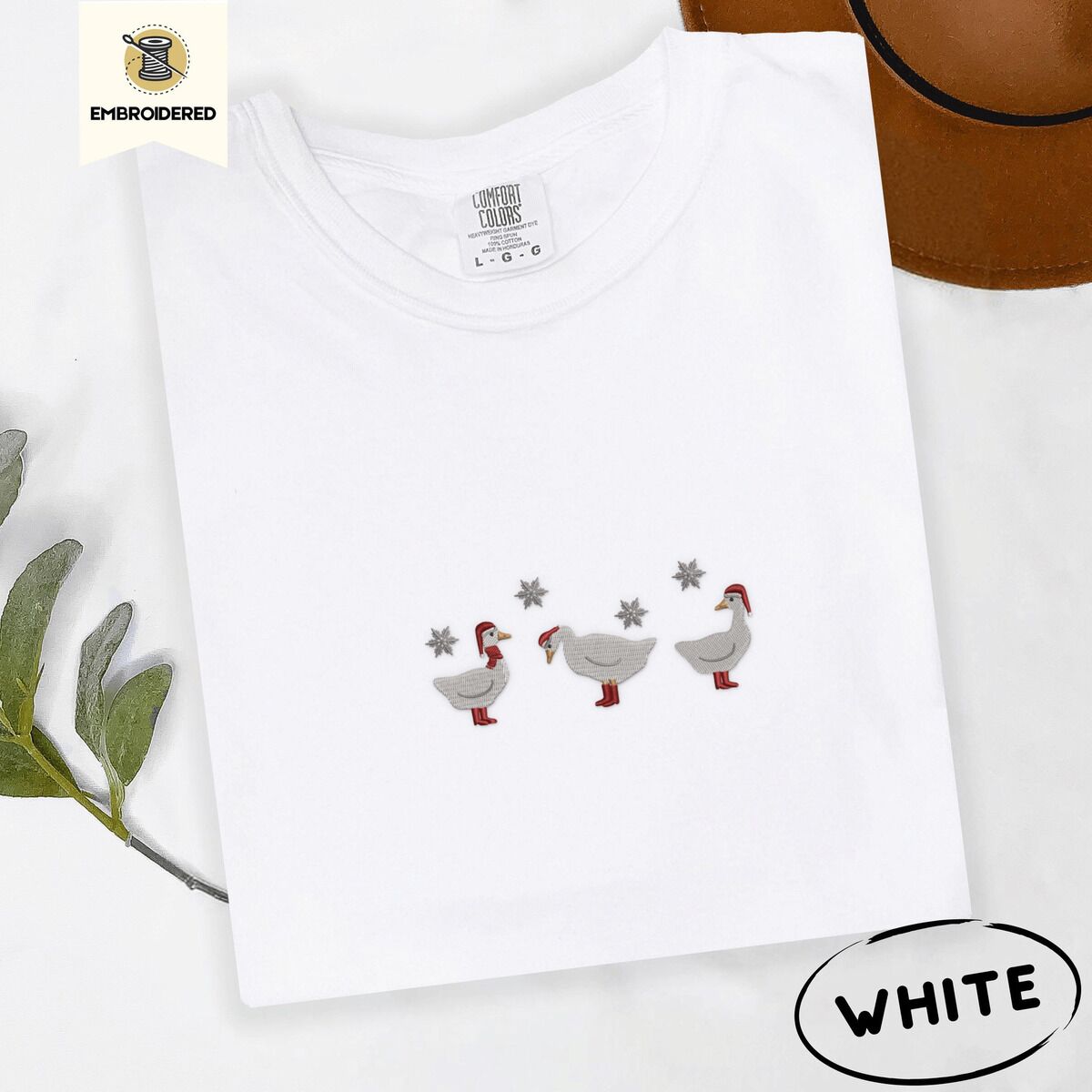 Duck in Boots Shirt – White White Comfort Colors T-shirt embroidered with three white ducks in Santa hats and red rain boots under silver snowflakes