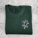 Electrocuted cat crewneck in Forest Green with the shocked black cat and colorful Christmas light bulbs on the left chest