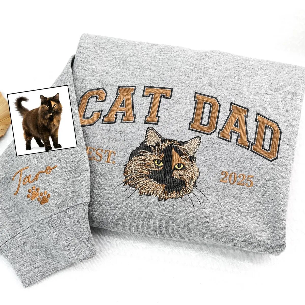 Embroidered Cat Dad Sweatshirt – Sport Grey Sport grey sweatshirt with copper CAT DAD lettering, an embroidered tortoiseshell cat face, EST. 2025 and the name Taro with paw prints on the sleeve