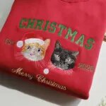 Close-up of embroidered orange and black cat portraits under green varsity CHRISTMAS lettering