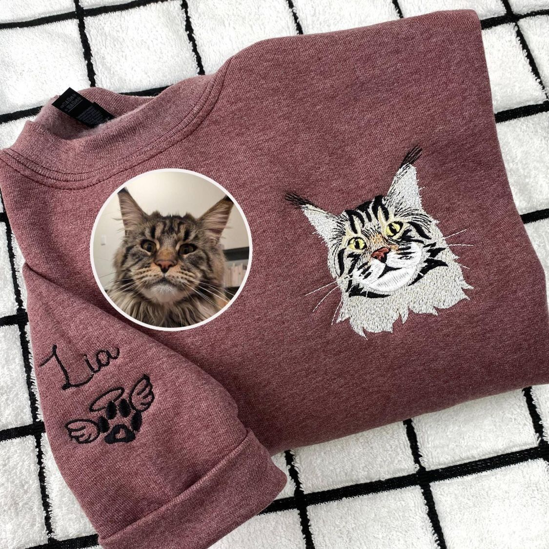 Embroidered Cat Sweatshirt – Memorial Portrait with Angel Paw Sleeve Maroon heather embroidered cat sweatshirt with a long-haired tabby cat portrait on the chest and the name Lia with an angel paw on the sleeve, beside the original photo