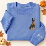 Embroidered Doberman Halloween sweatshirt in Heather Deep Royal with a witch-hat Doberman Pinscher holding a pumpkin bucket on the left chest