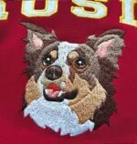 Embroidered dog face sweatshirt detail with white varsity name letters outlined in gold above the portrait