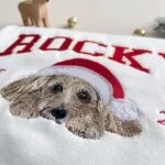 Close-up of the embroidered dog portrait and red Santa hat on a personalized Christmas sweatshirt