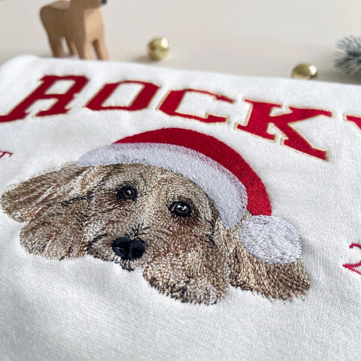 Embroidered Dog Portrait in a Santa Hat – Close-up Close-up of the embroidered dog portrait and red Santa hat on a personalized Christmas sweatshirt