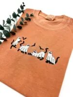 Angled close view of black cats in white ghost sheets with flying bats embroidered on a yam tee