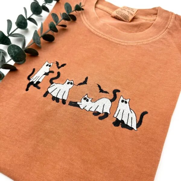 Angled close view of black cats in white ghost sheets with flying bats embroidered on a yam tee